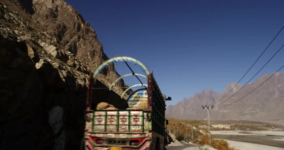 A colorfully painted truck travels along a narrow road through the dry mountainous countryside on a sunny day