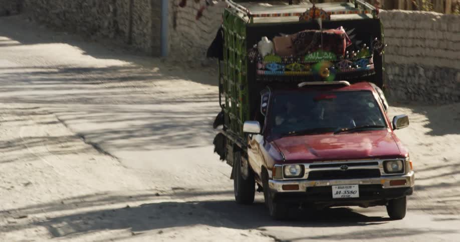 Truck with full truck bed drives past wall of stacked blocks and passes goat