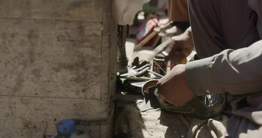A man threads new leather as he repairs a shoe outdoors