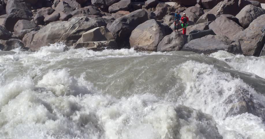 Two people standing on the rocks near the turbulent waters of a river rapids
