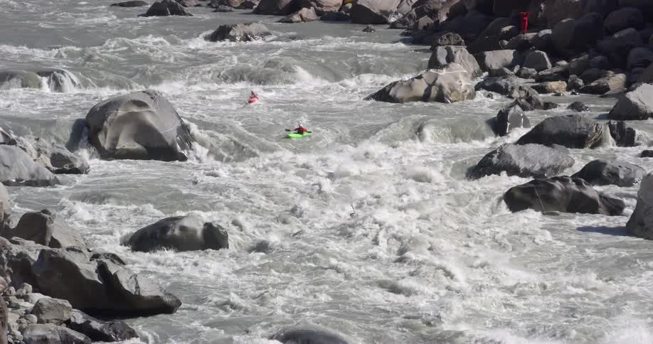 Person stands on shore watching people paddle kayaks down whitewater rapids