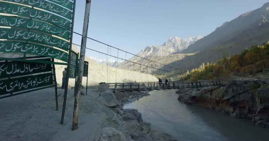 People walk across bridge over river by mountains in middle eastern area