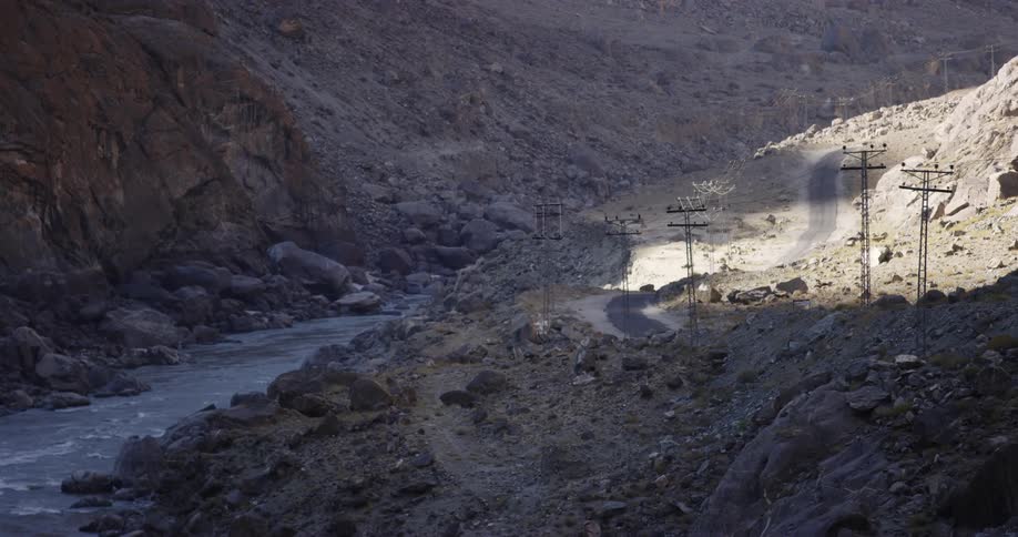 A small river and a road run through the stone strewn valley of a mountain during the day