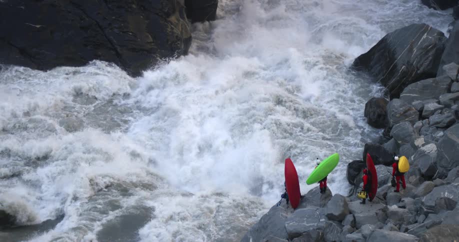A group of kayakers stand on rocks on the side of a river while holding their kayaks