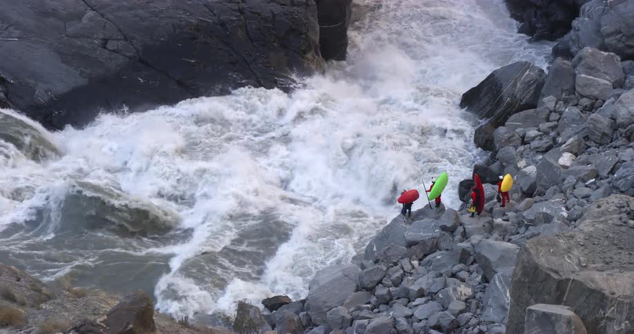 A large waterfall runs down into a river with people standing beside it with canoes