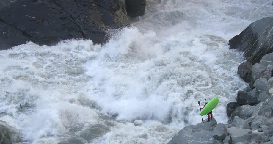 A person with a kayak and a paddle standing on the rocks next to a river