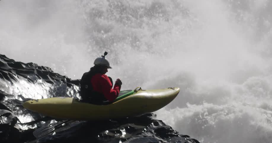 A person in a kayak on a rock in a river