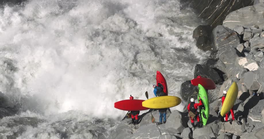 Group of people with kayaks stand next to whitewater rapids