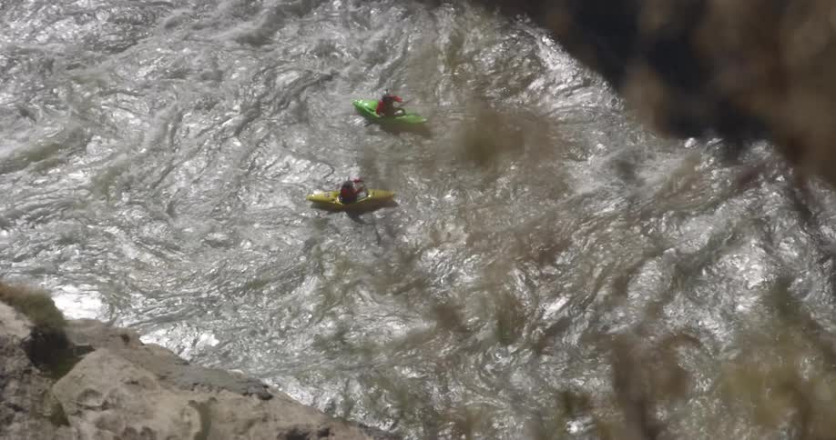 Two people paddling kayaks on the turbulent river rapids