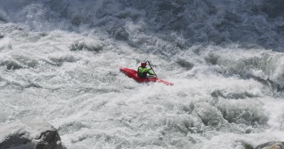 A kayaker paddles their kayak through the violent rapids of a river
