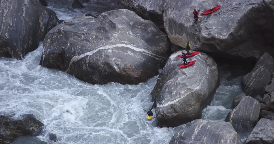A person sitting in a kayak on a large rock slides off the rock in to the river below to ride the rapids
