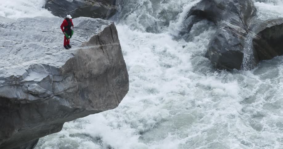 A person stands on the ledge of a rock formation watching rapids below