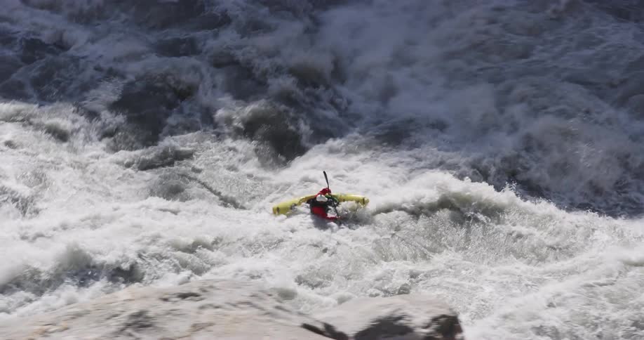 Man in a yellow kayak paddles through the turbulent waters of a river rapids