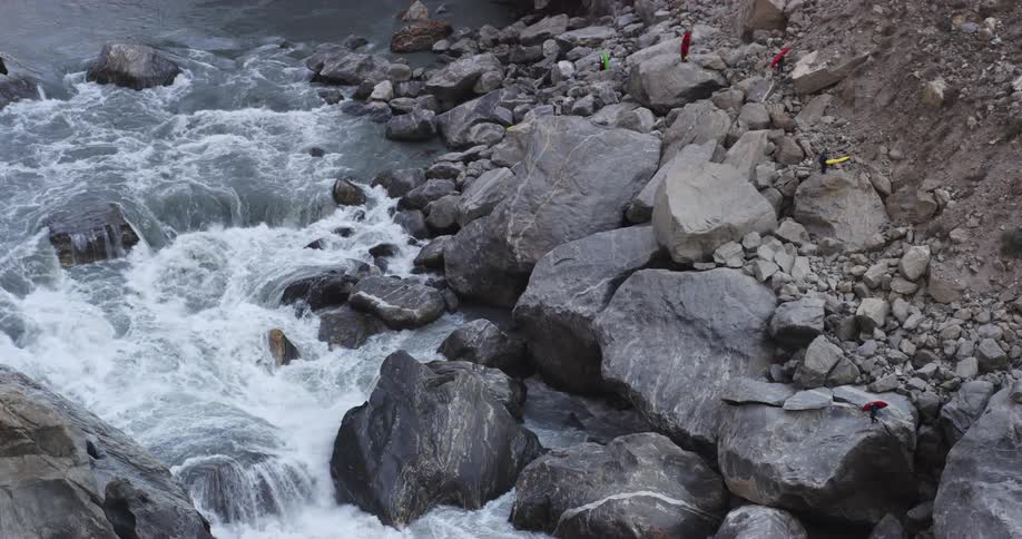 A group of kayakers carry their kayaks as they stand on boulders next to a river