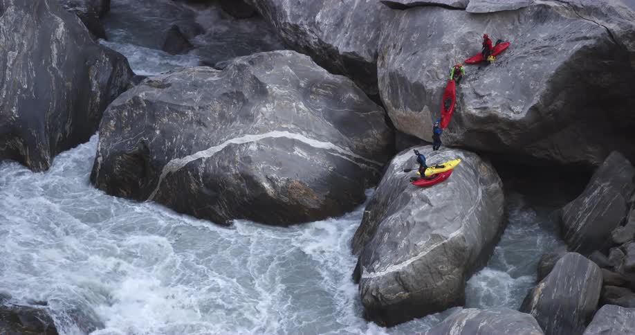 People carrying their kayaks down large rocks towards a river with rapids