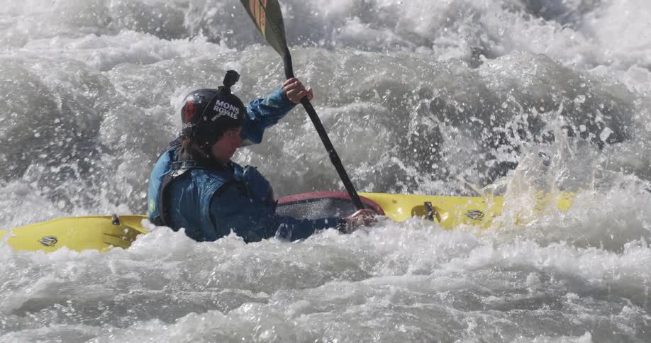 Man aboard a yellow kayak paddles on the turbulent waters of a river