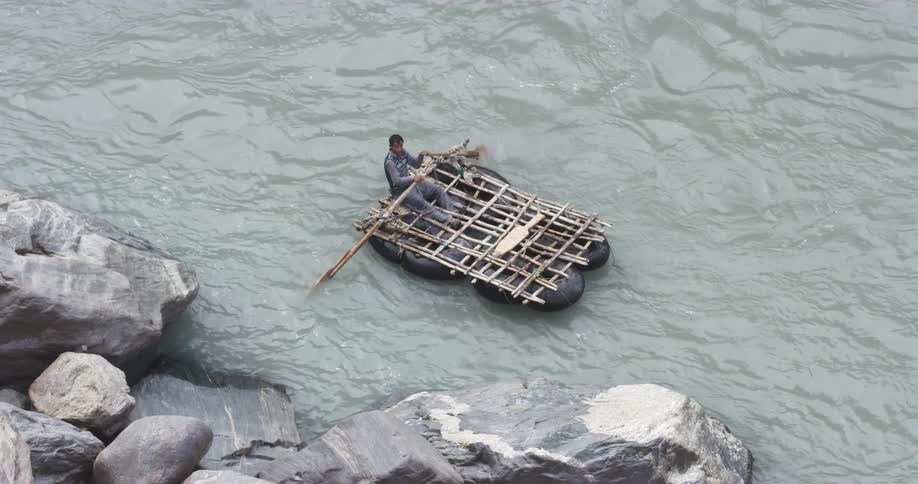 Person on homemade raft in ocean using oars to paddle