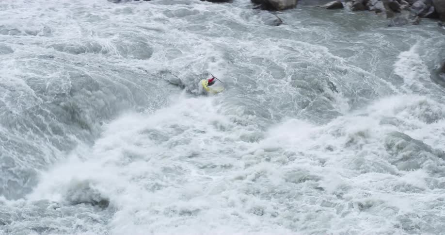 A kayaker attempts to navigate the violent waters of a rocky river during the day