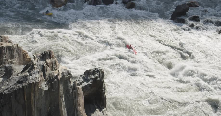 Two people with canoes and paddles going down a river with rocks