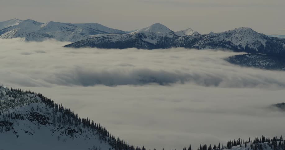 A mountain range with snow and trees with the sky and clouds in the background