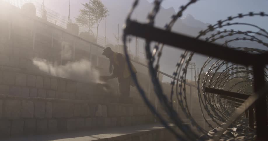 A man sweeps off stone steps behind a fence with coils of barb wire at the top