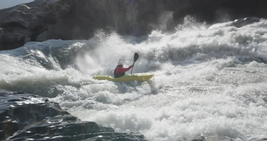 Person paddles kayak along whitewater rapids away from fog covered mountain side