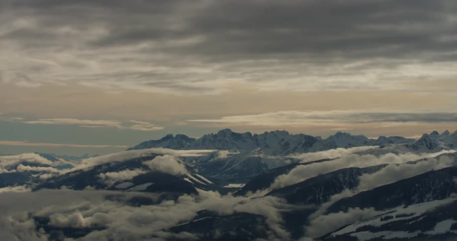 A mountain ridge covered in both snow and fog under a cloudy sky