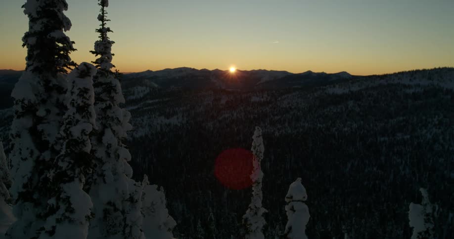 The sun shining over a snowy mountain range in winter