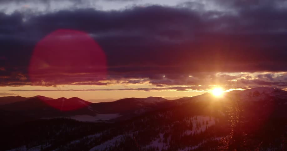 The sun goes down behind the mountains on the horizon with dark clouds