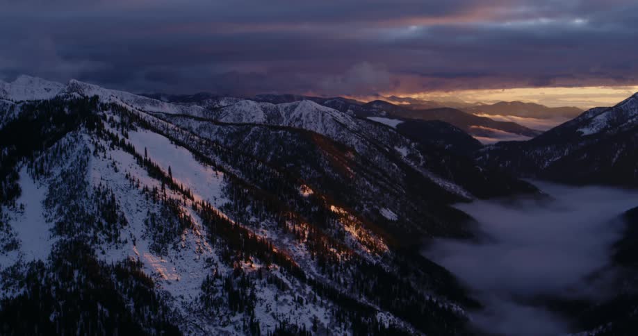 Clouds over a valley on the snow covered mountains at sunset