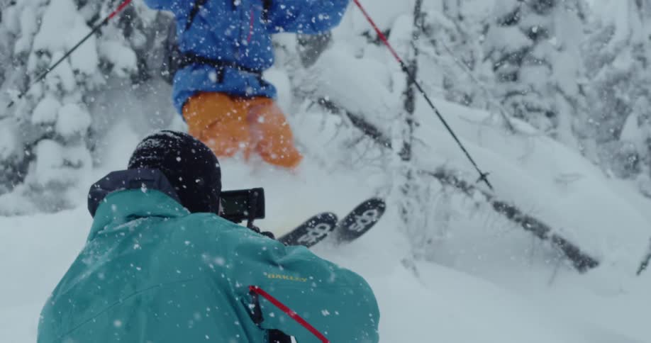 A person holds a video camera as a person does a ski jump in front of them
