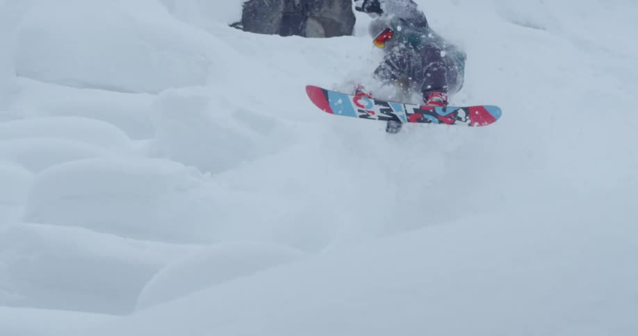 Snowboarder jumps and spins while traveling down snowy slope