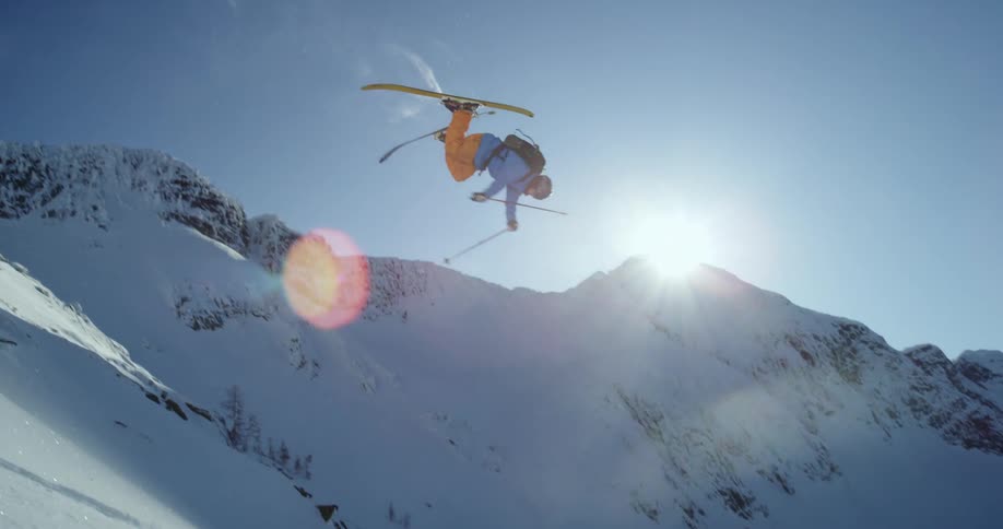 A man skiing down a mountain performs a back flip on a bright and sunny day