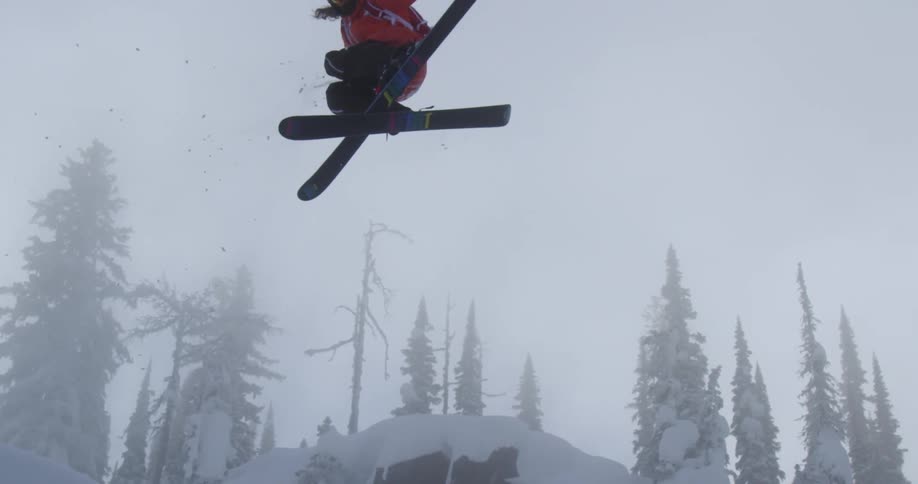 A skier does a large turning jump over a snow covered rock