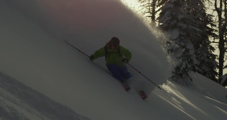 Fresh powder billows behind a skier skiing down a steep mountain slope