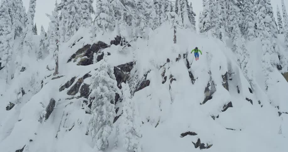 A skier jumping off a cliff in snowy mountains on a winter day