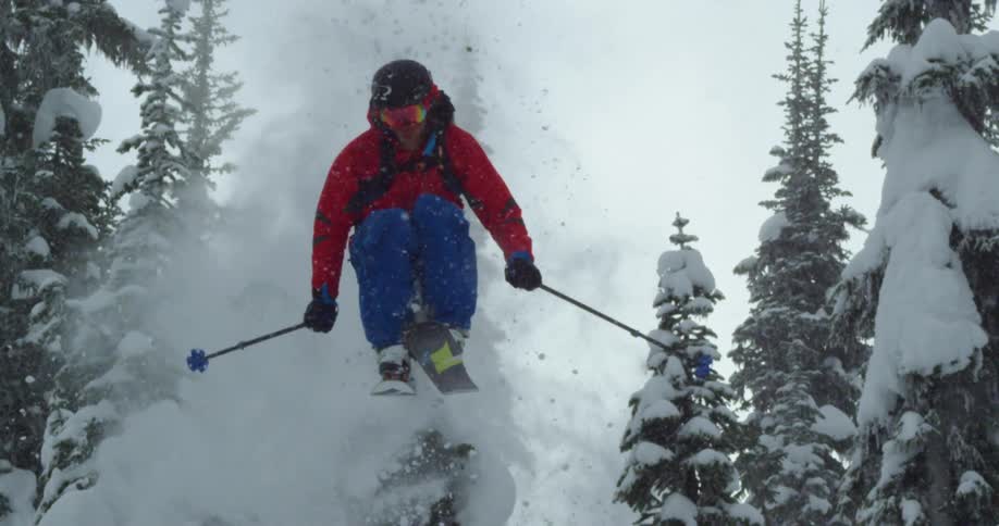 A skier going off a jump in a mountain forest on a snowy day