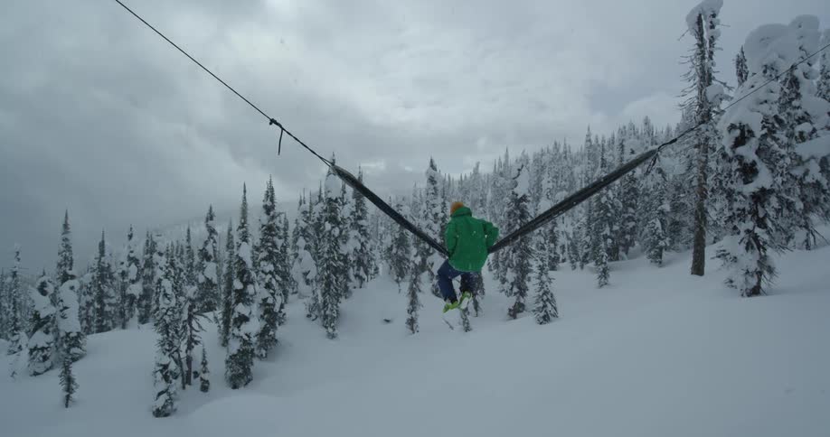 A person in a snow covered forest swings on a large piece of material stretched between ropes