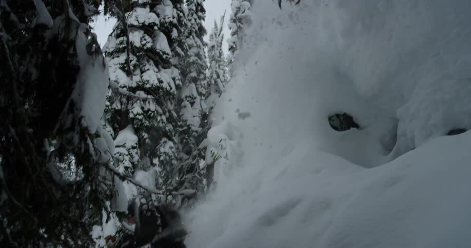 A person wearing snow gear and skis is skiing down a snowy hillside with trees surrounding it