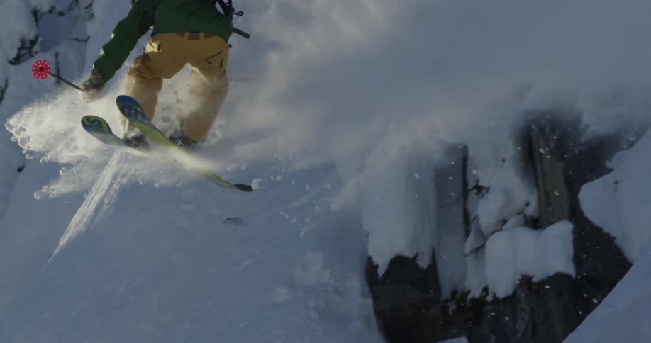 A person with a backpack helmet and goggles skiing and jumping down a snowy slope