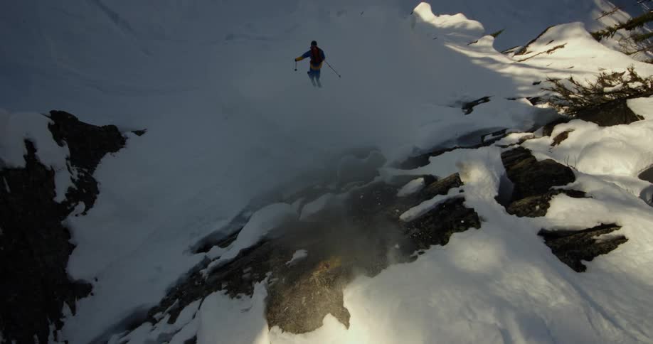 A person with a backpack and a helmet skiing and jumping off a snow covered mountain