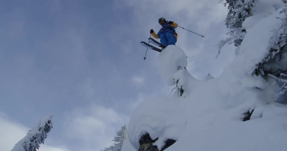 Skier jumps over the snow covered trees on a slope in the mountains near a pine forest