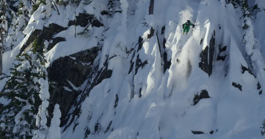 Person makes ski jump from cliff in snowy mountains