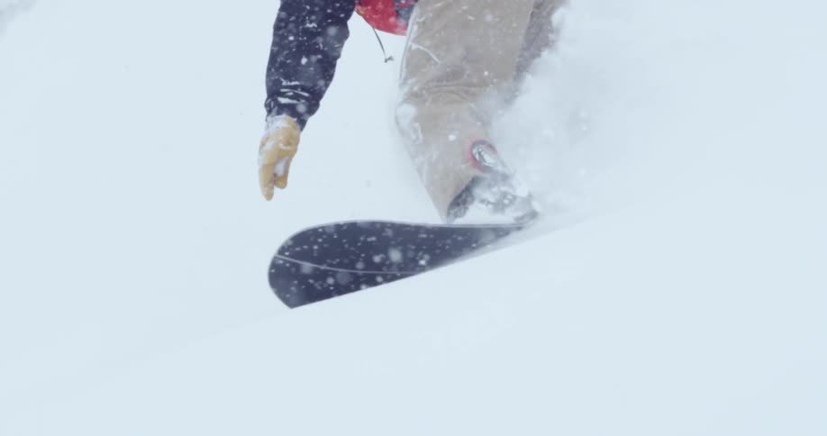 A snowboarder kicks up snow while going down the side of a mountain