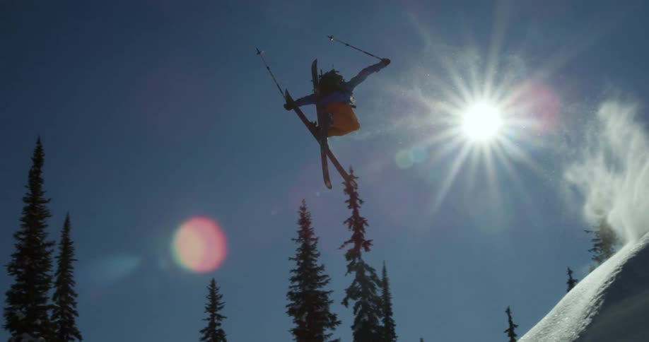A skier spins in midair after flying of a mound of snow before landing on and continuing down a snowy mountain slope