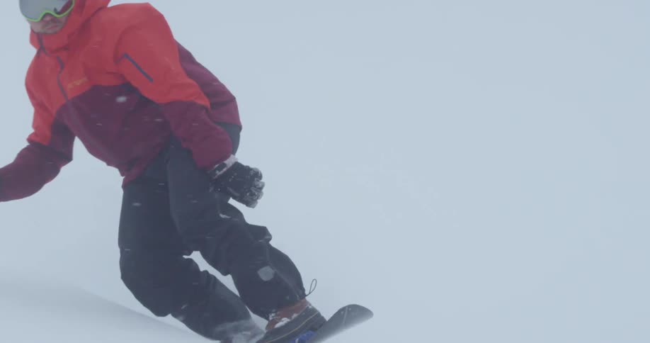 A snowboarder rides down a mountain slope as snow falls from the sky
