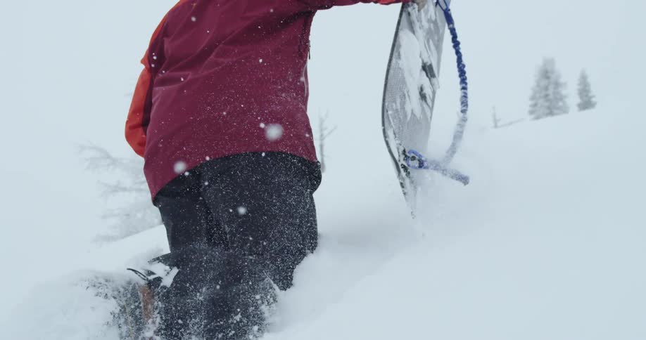 A snowboarder carries a snowboarder as they attempt to climb a mountain slope covered in deep snow