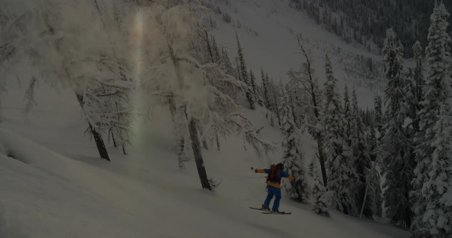 A skier falls through air onto a steep mountain slope and attempts to keep their balance as they slide towards a group of trees