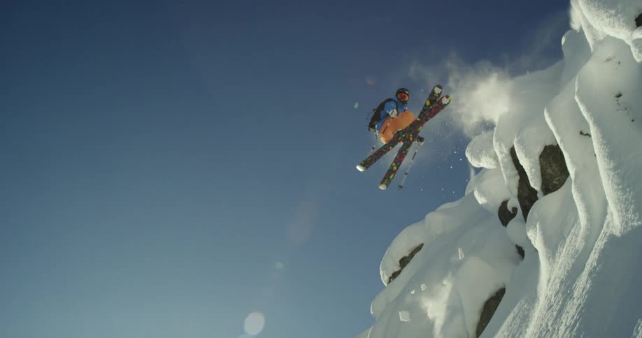 A skier spins as they fall off a cliff and lands backwards on the slope below