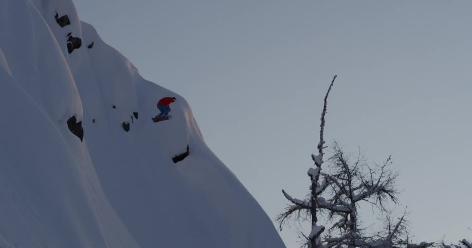 A person snowboarding and jumping on a snow covered mountain with trees